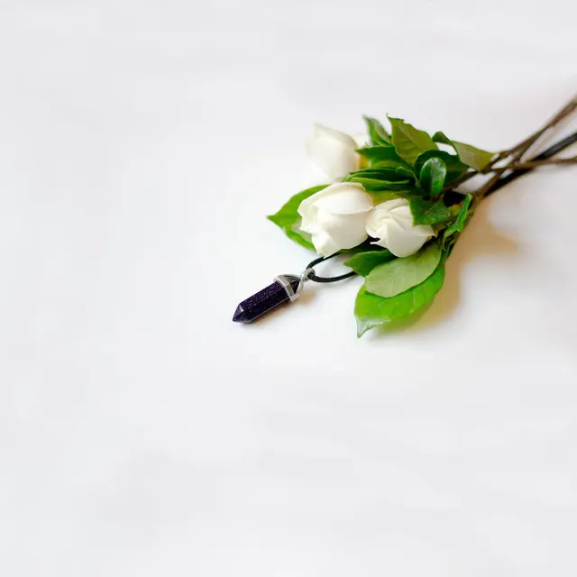 Elegant white roses and amethyst crystal pendant on a white surface.