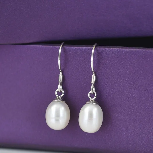 Close-up of exquisite white pearl earrings displayed against a luxurious purple box.
