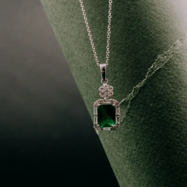 Close-up of an elegant emerald pendant necklace with silver chain, showcasing sophistication and style.