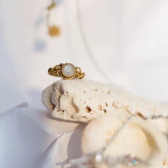 Close-up of an elegant gold ring with a gemstone, displayed on a natural stone background.