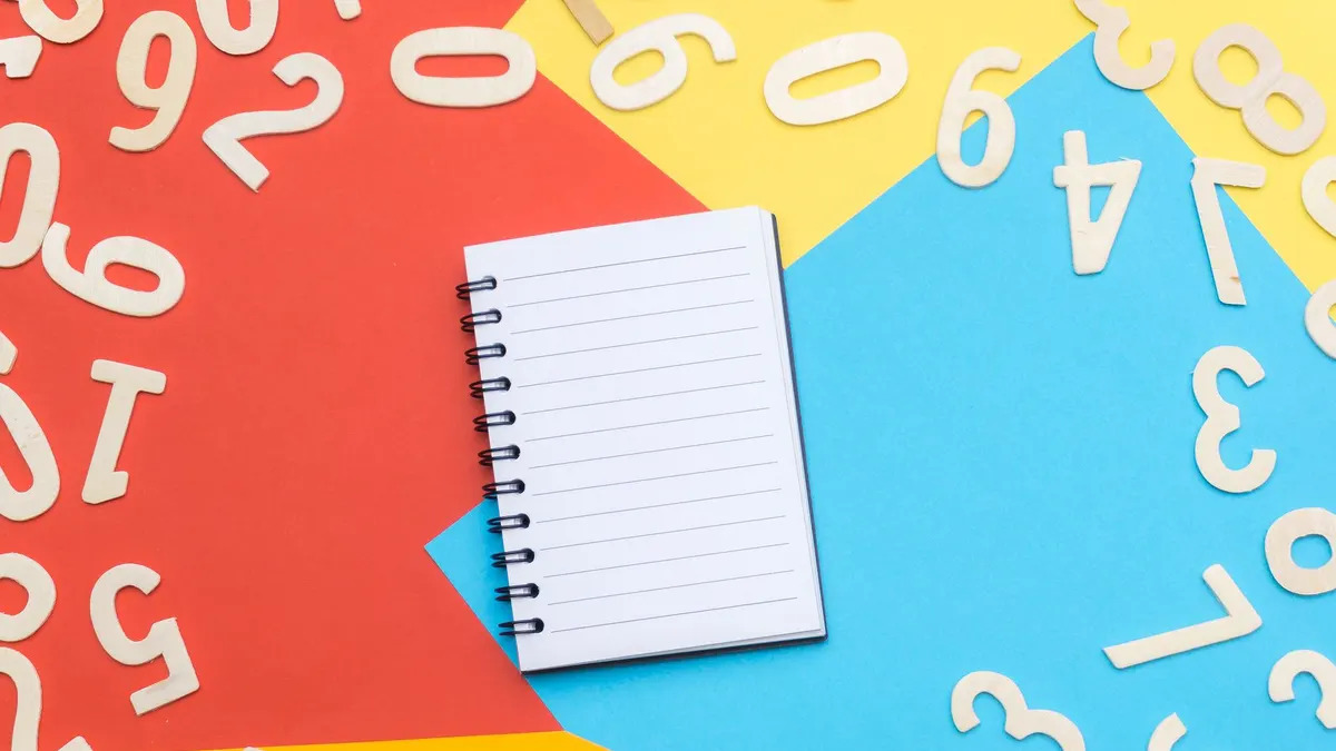 A spiral notebook surrounded by wooden numbers on a colorful geometric background, featuring red, yellow, and blue.