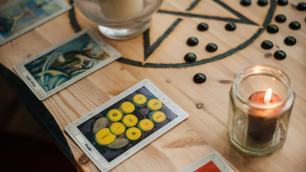 From above of shiny candle in jar near bright tarot cards with illustrations on wooden table with oracle symbol