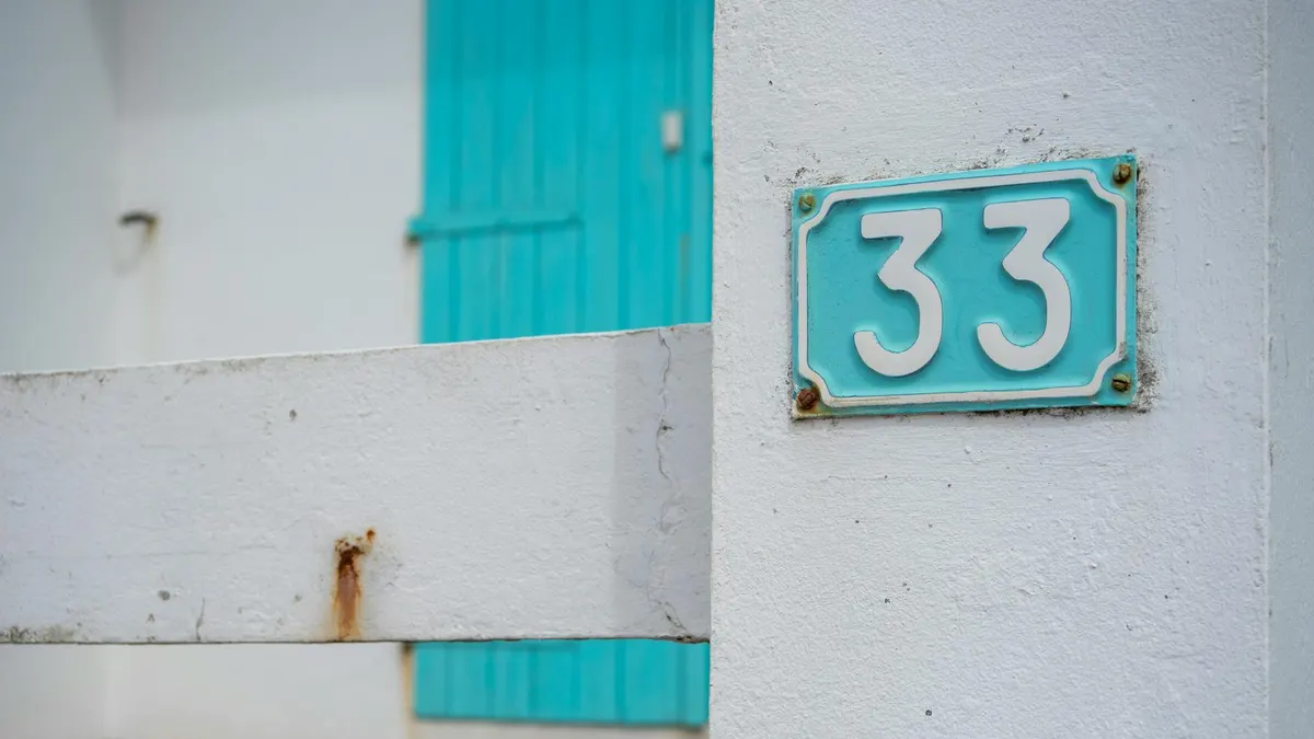 Close-up of a white wall with a turquoise number 33 sign, outdoor setting, minimalistic style.