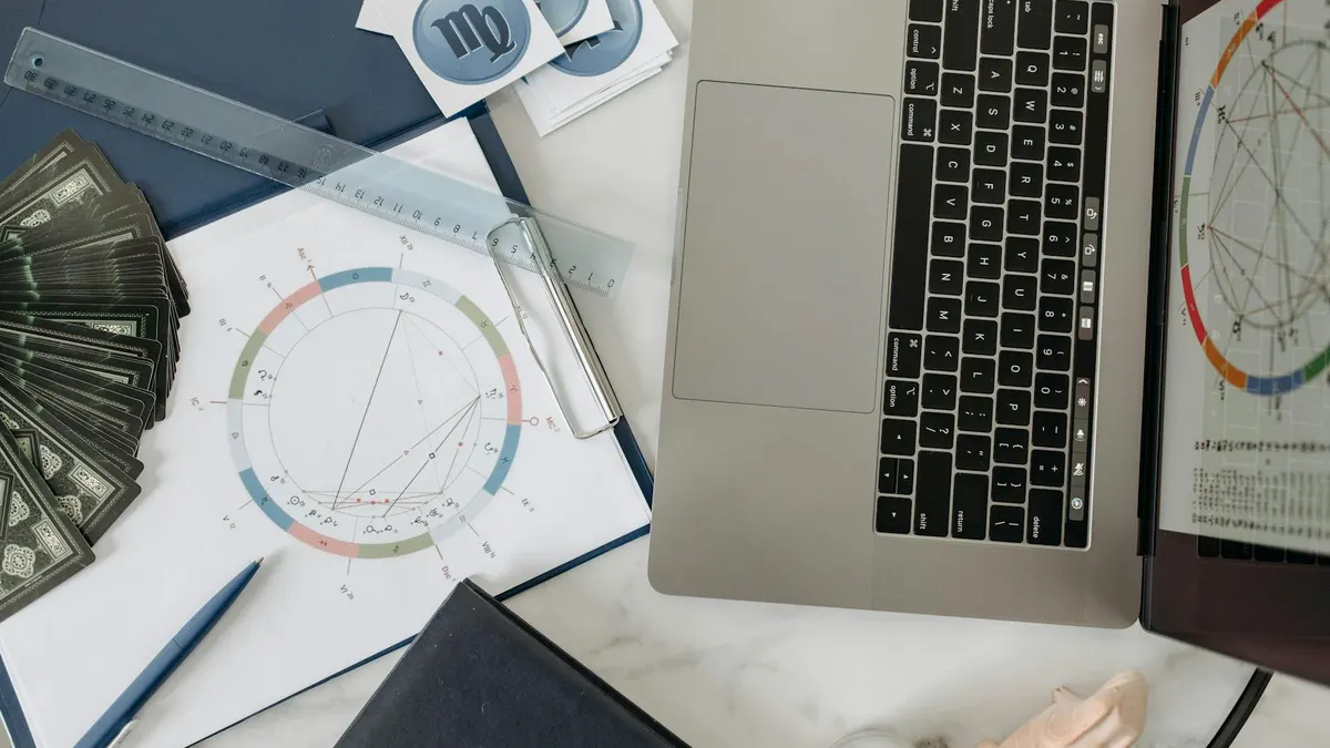 Astrology chart, laptop, and tarot cards on a desk, study of celestial influences.