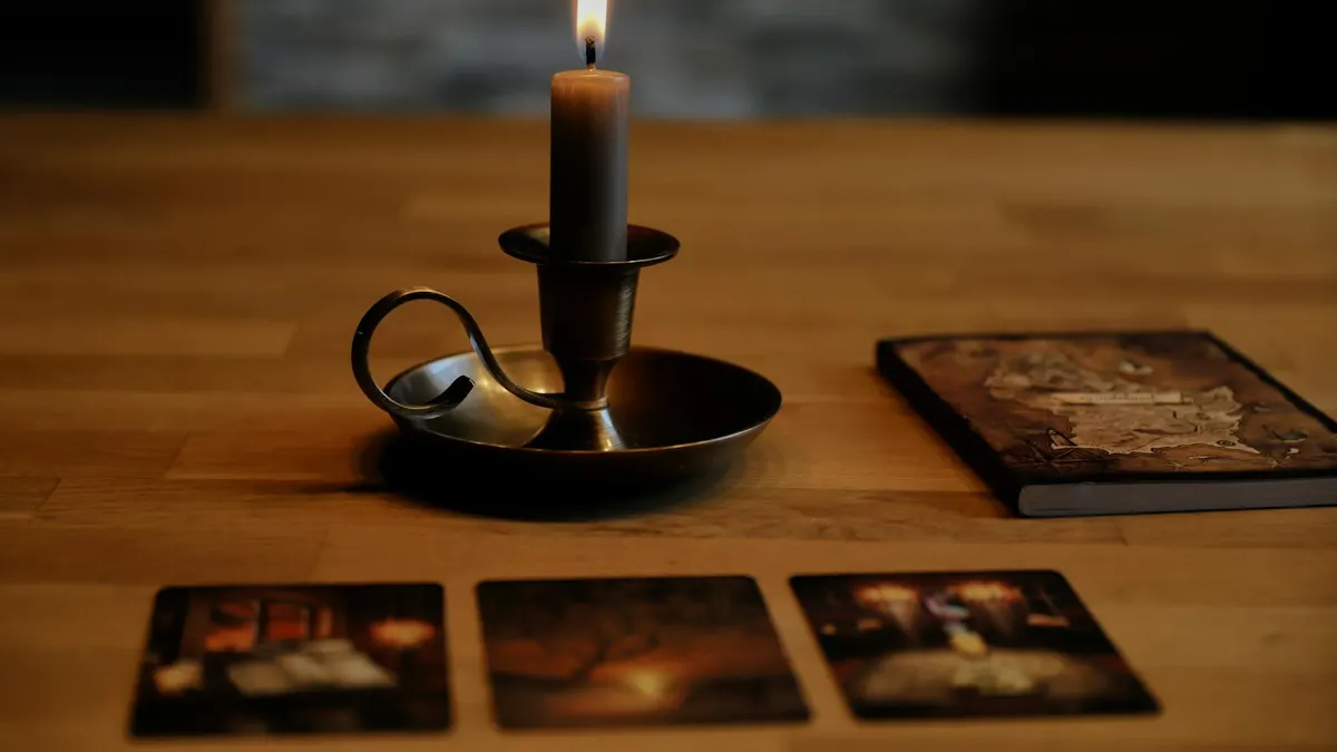 Moody setup with candleholder, tarot cards, and aged book on wooden table.